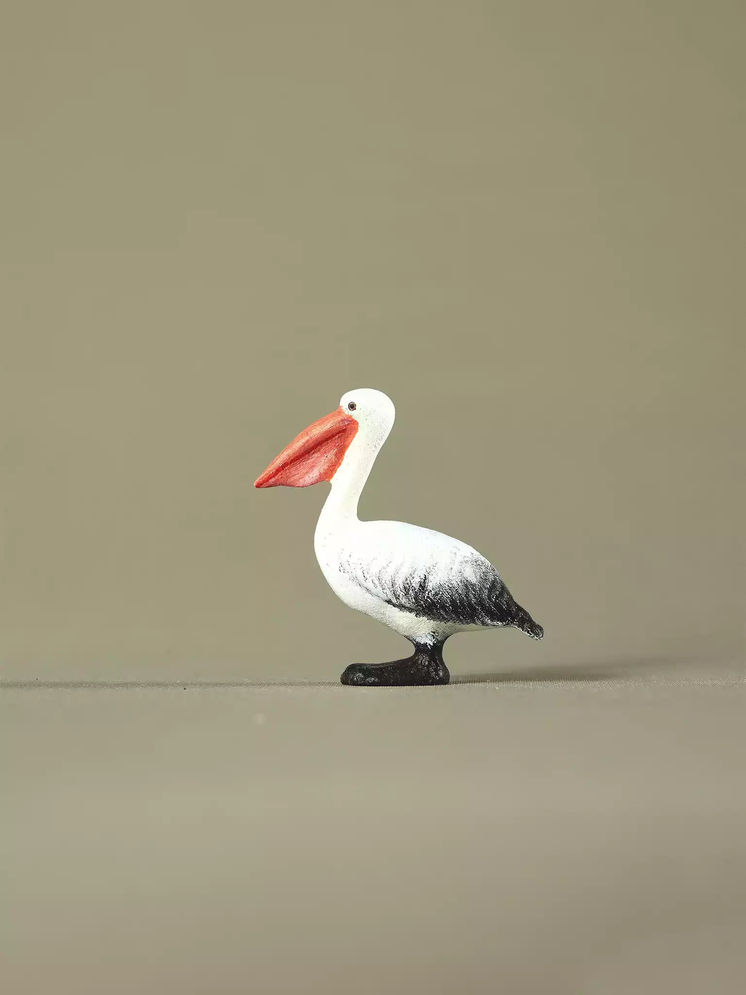 Wooden pelican toy facing right, displaying hand-painted details and a soft black, white, and orange color palette.