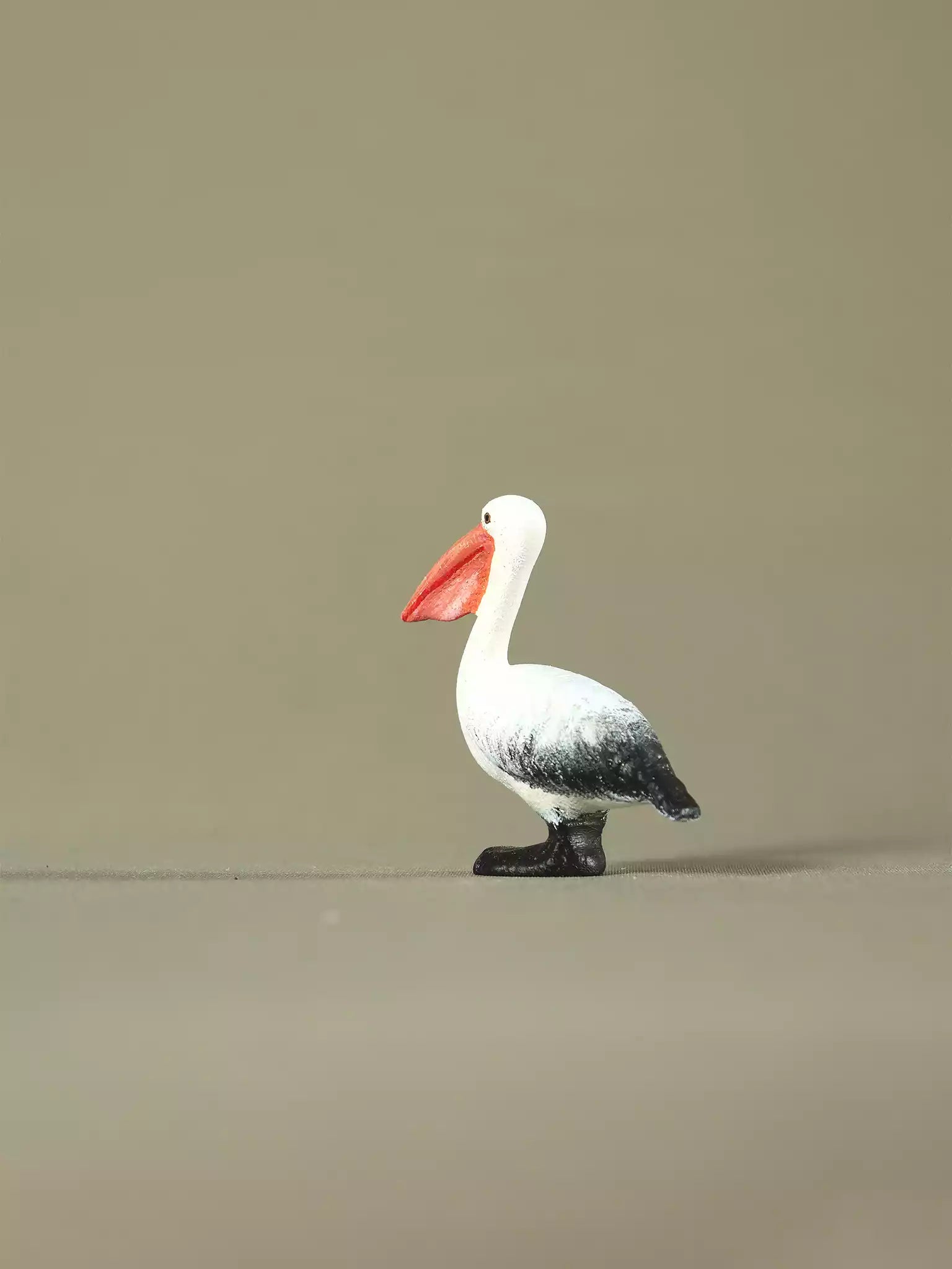Side view of a handcrafted wooden pelican figurine on a plain background, highlighting its curved neck and painted feathers.