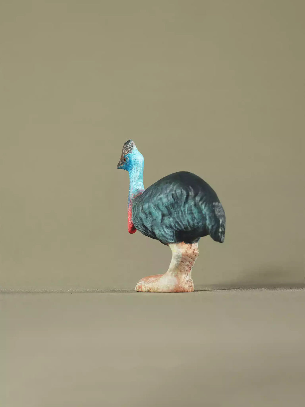Wooden cassowary collectible toy with carved body texture, photographed on a neutral surface.