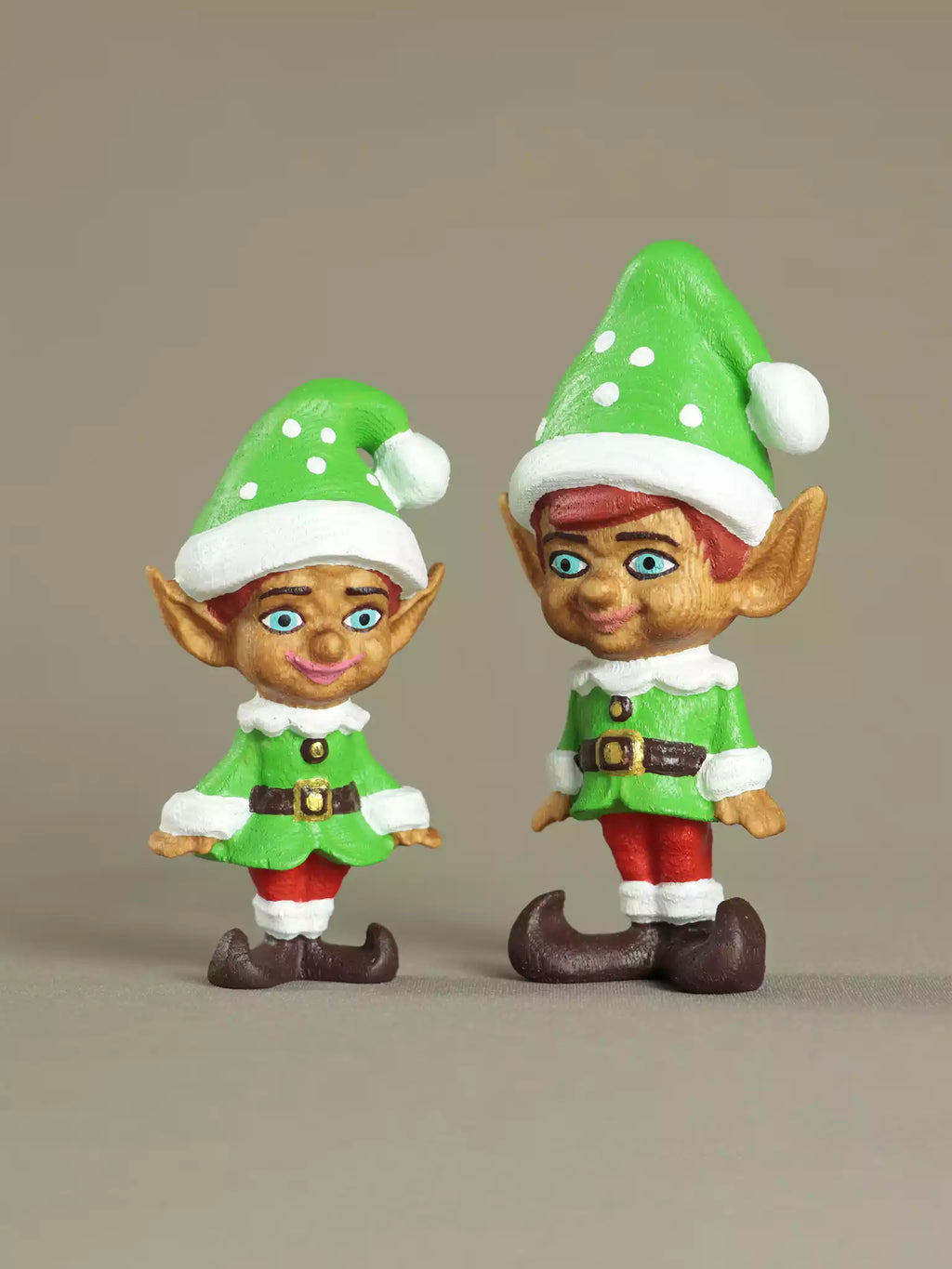 Two elf figurines with green hats and outfits on a beige background
