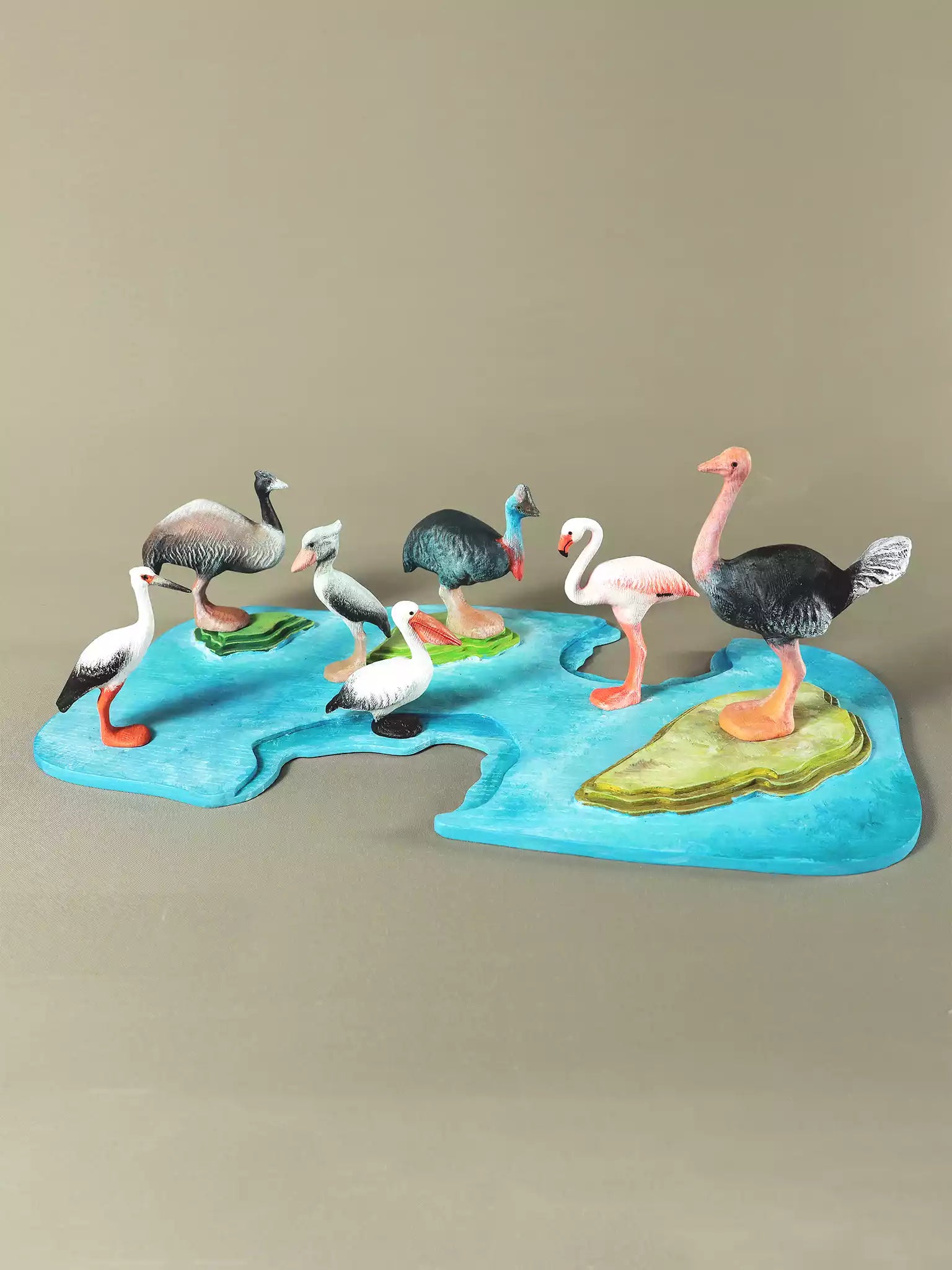 Set of seven wooden collectible birds displayed on a colorful map-like base, showcasing their detailed craftsmanship and vibrant colors.