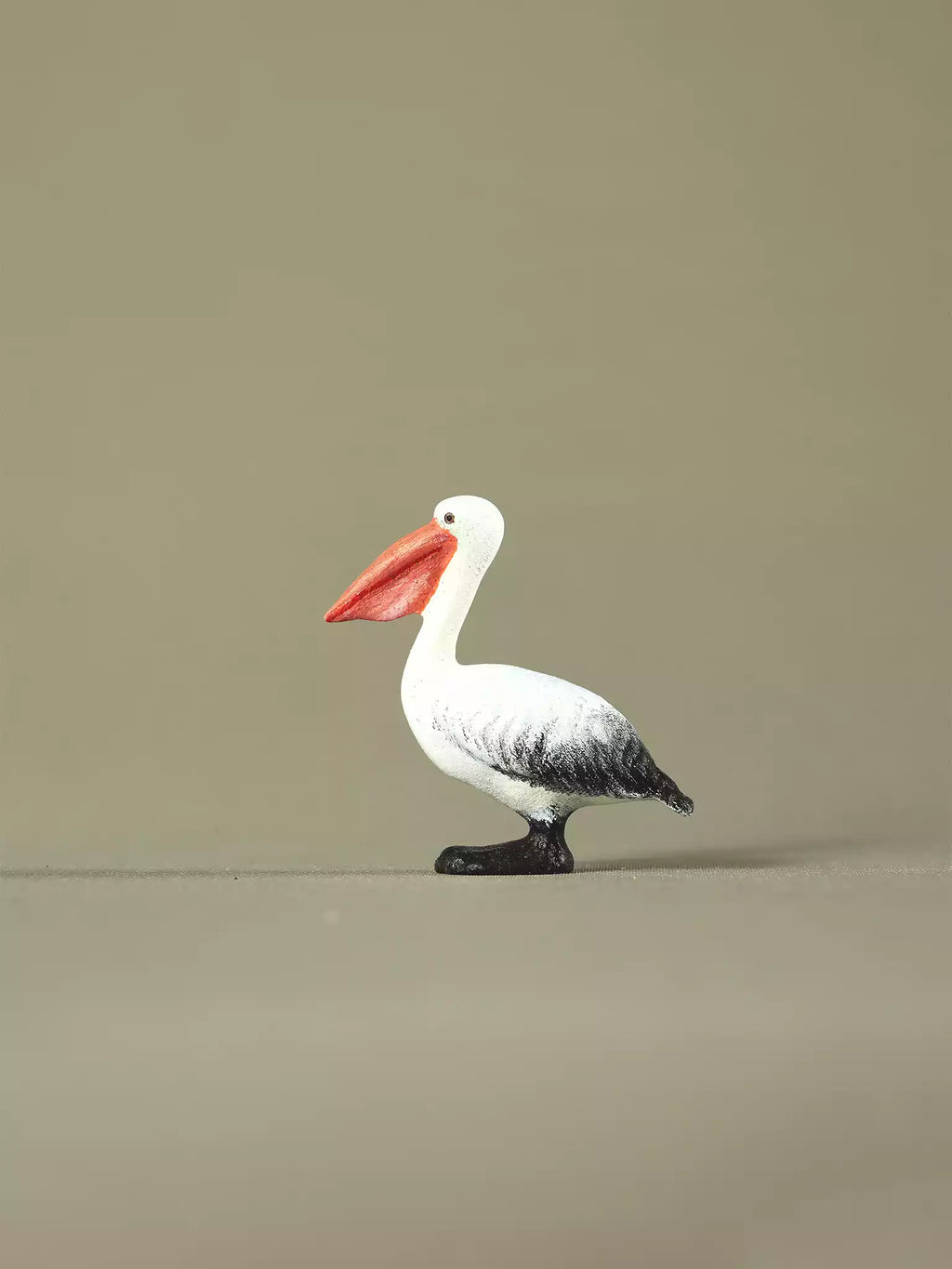Wooden pelican toy facing right, displaying hand-painted details and a soft black, white, and orange color palette.