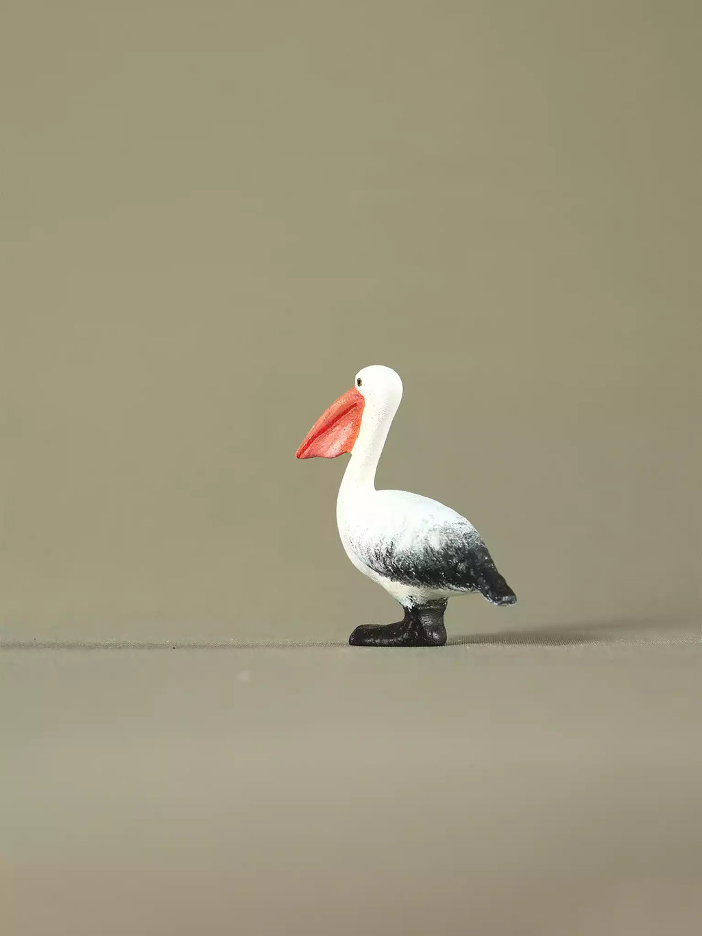 Side view of a handcrafted wooden pelican figurine on a plain background, highlighting its curved neck and painted feathers.