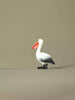 Side view of a handcrafted wooden pelican figurine on a plain background, highlighting its curved neck and painted feathers.