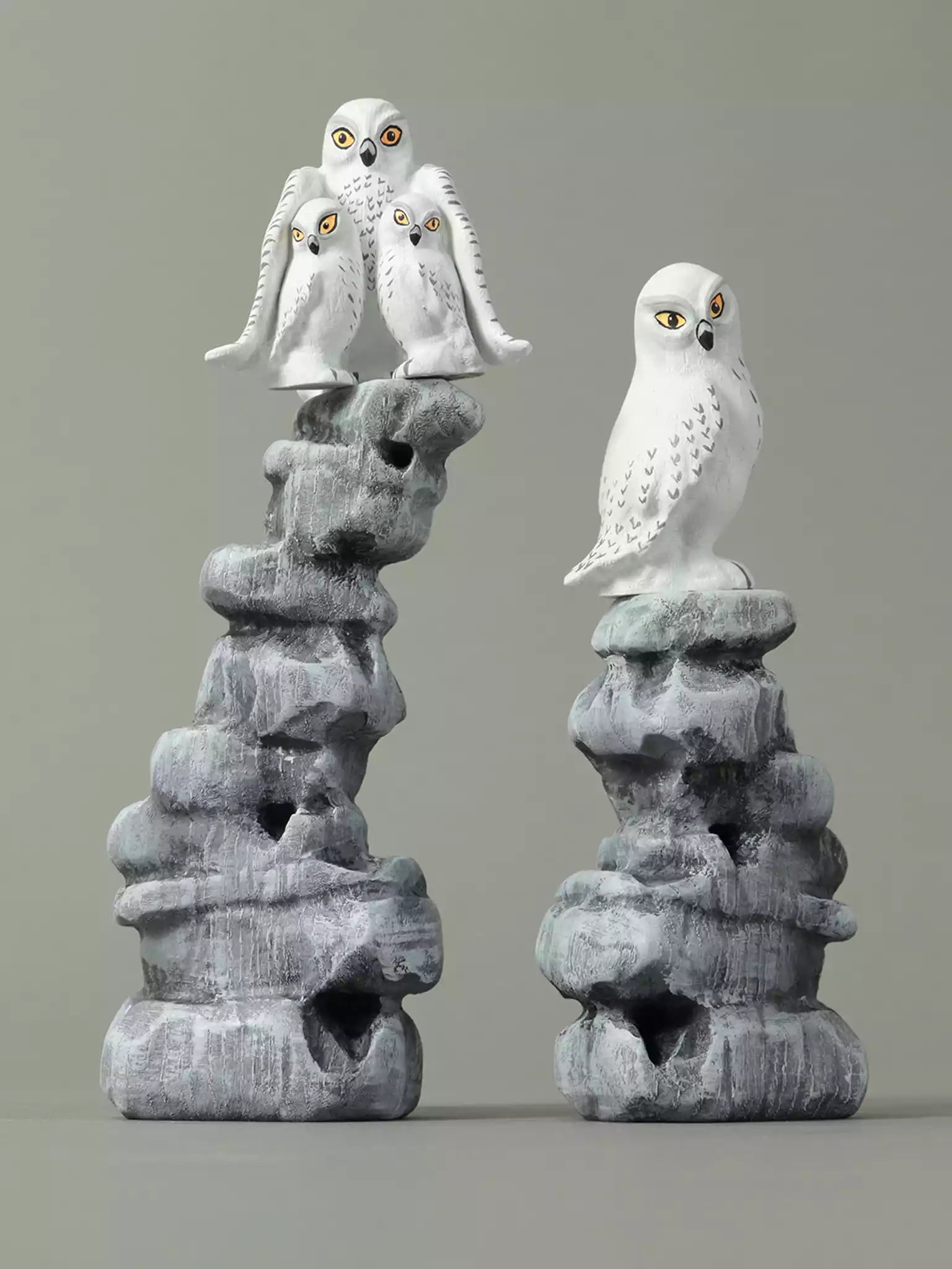 Two stone sculptures of snowy owls on gray rock bases against a gray background
