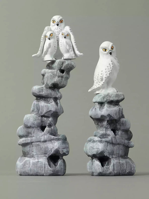Two stone sculptures of snowy owls on gray rock bases against a gray background