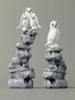 Two stone sculptures of snowy owls on gray rock bases against a gray background