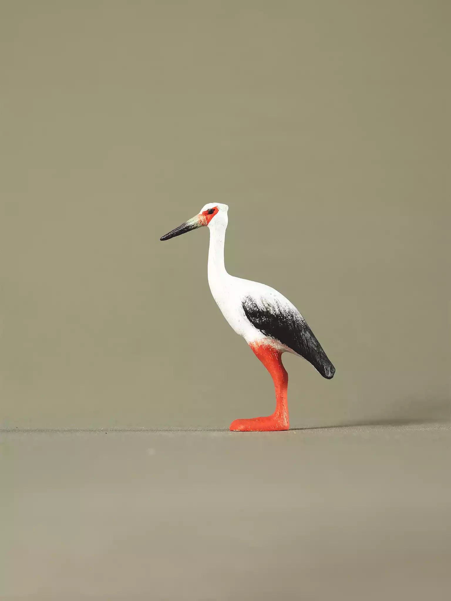 Side profile of a wooden stork figurine with a long beak, detailed wing painting, and bright orange legs.