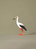 Side profile of a wooden stork figurine with a long beak, detailed wing painting, and bright orange legs.
